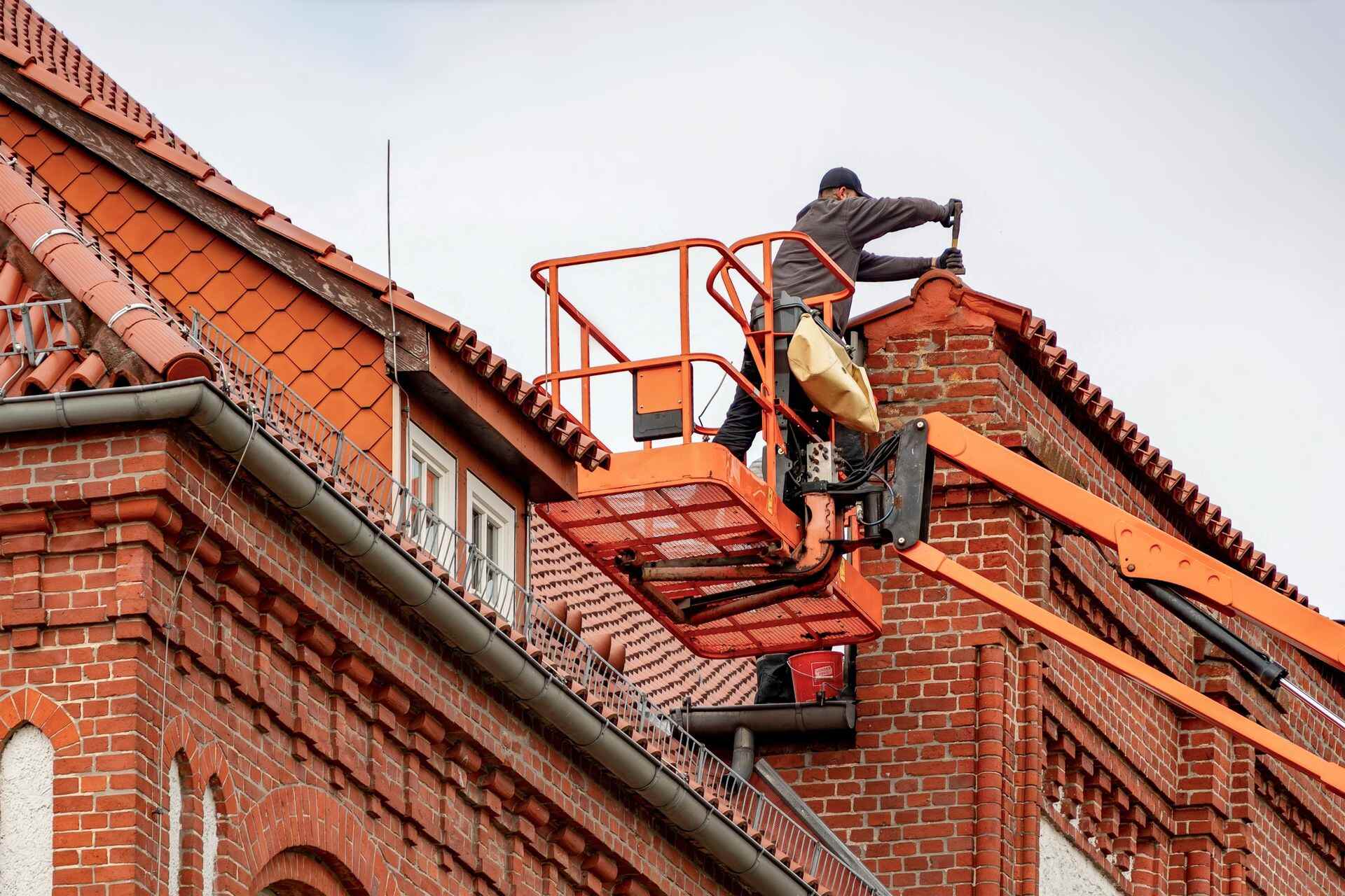 Technicien en nacelle intervenant sur la toiture et la façade en brique d'un immeuble