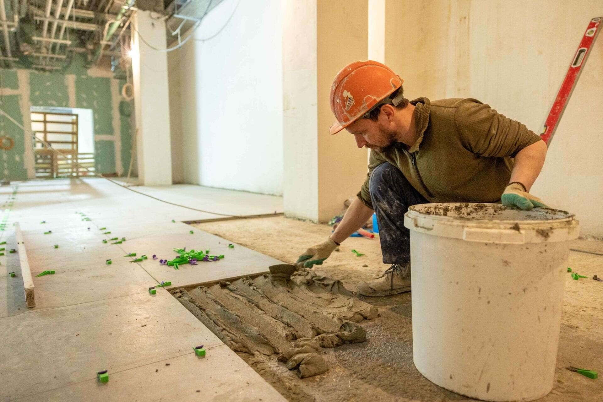 Carreleur à genoux posant un carrelage au sol dans une pièce en rénovation
