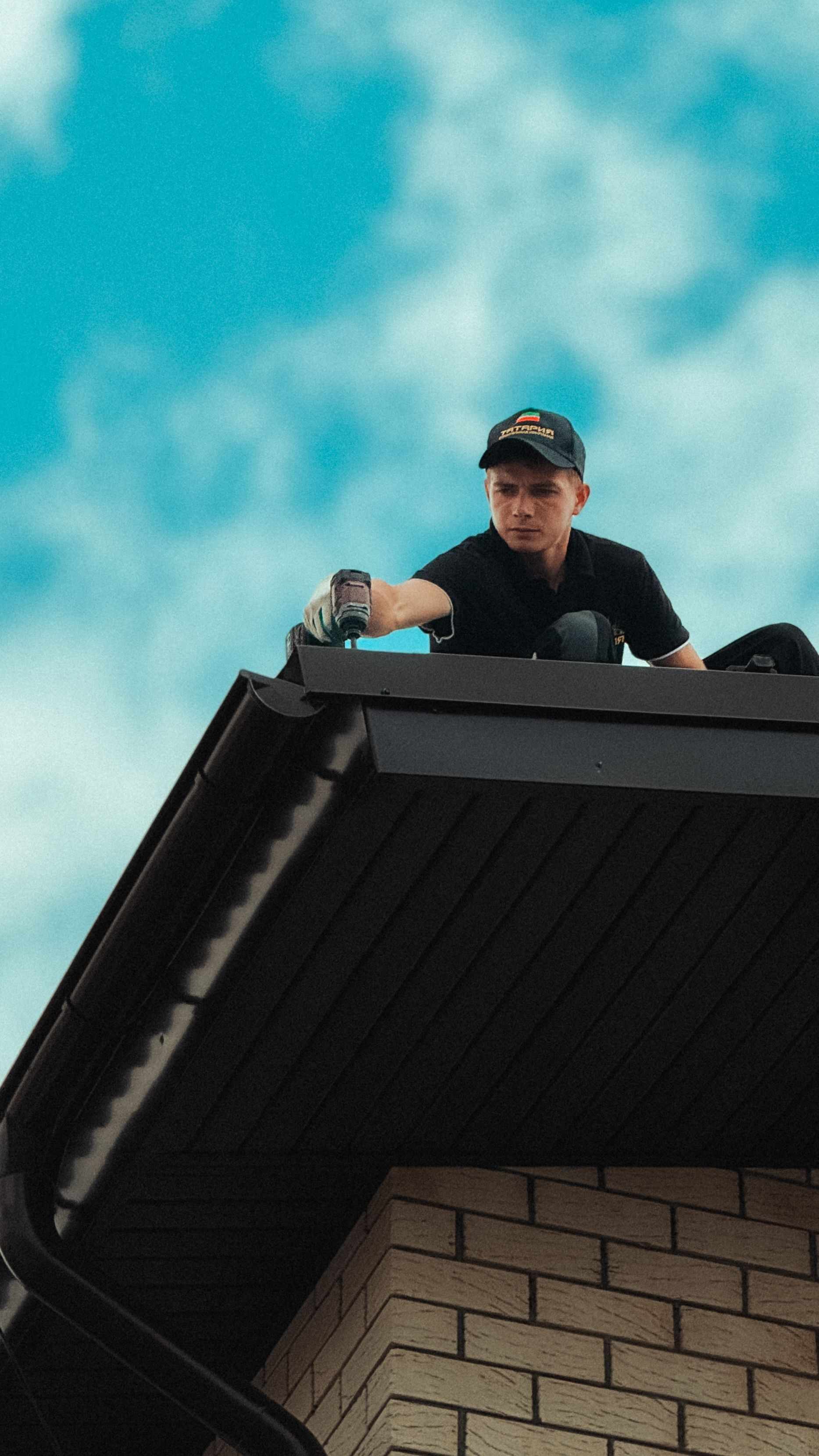 Couvreur au travail sur un toit, visseuse en main, sous un ciel bleu