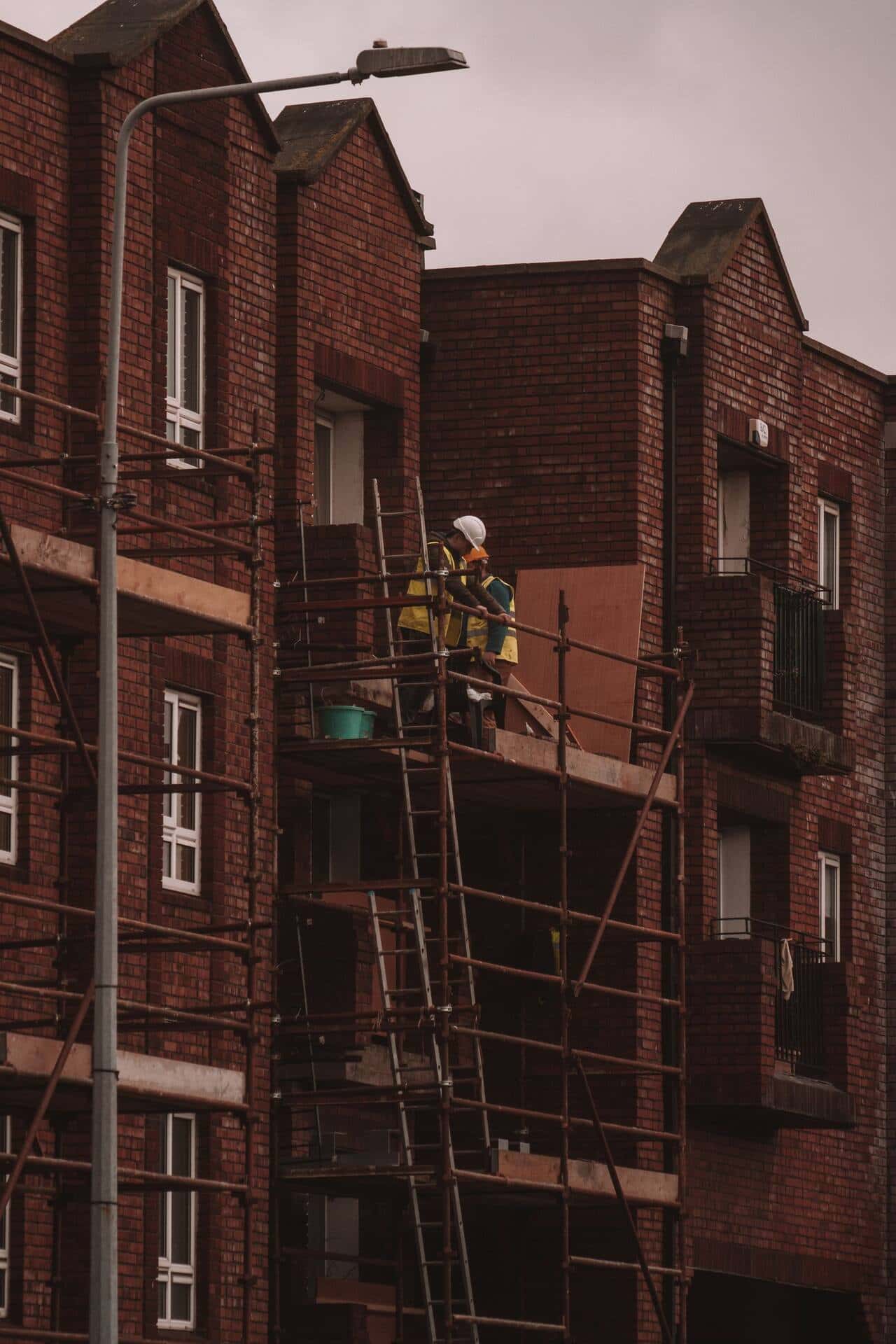 Ouvrier sur un échafaudage devant un immeuble en brique en rénovation