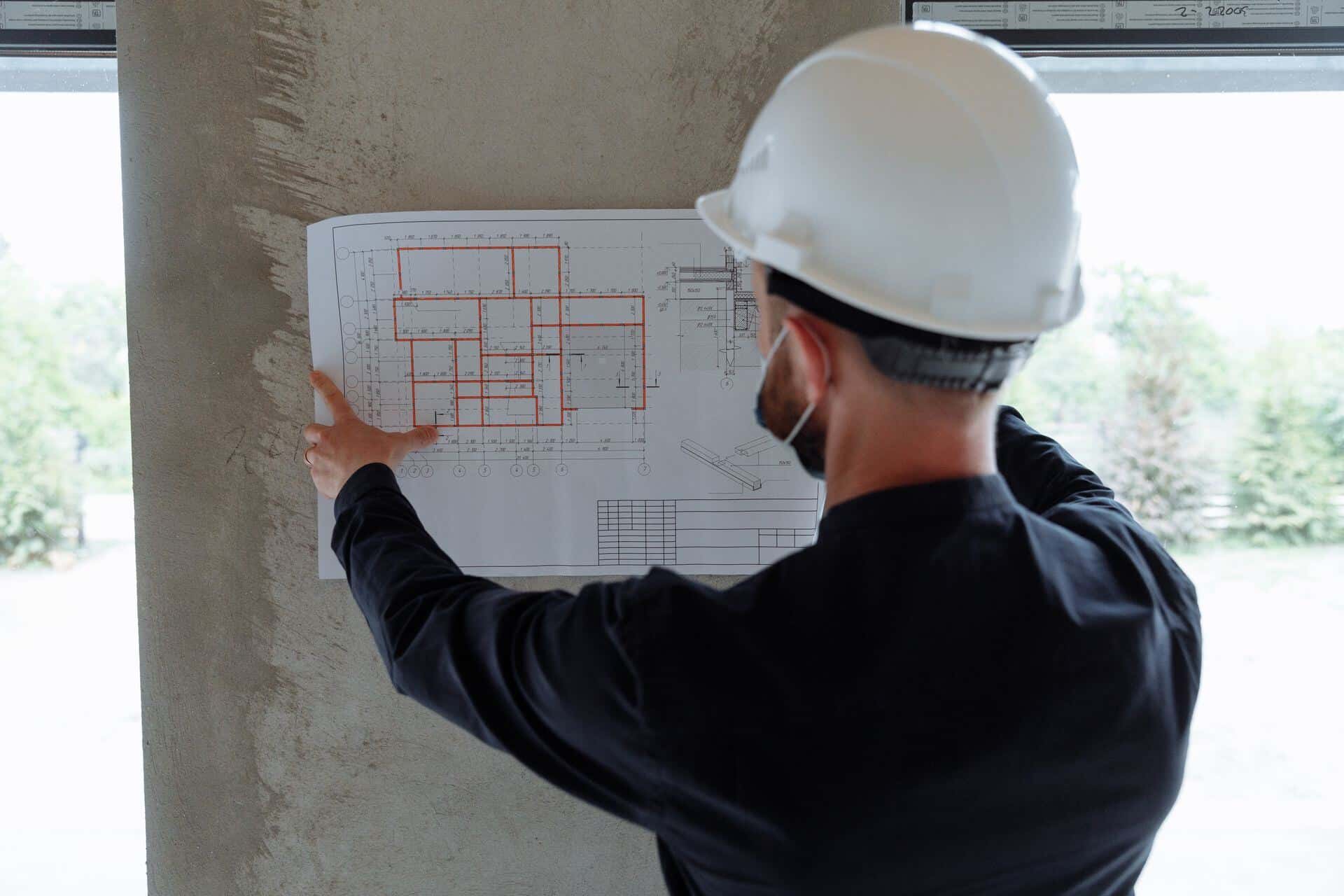 Maître d'œuvre casqué lisant les plans devant le chantier