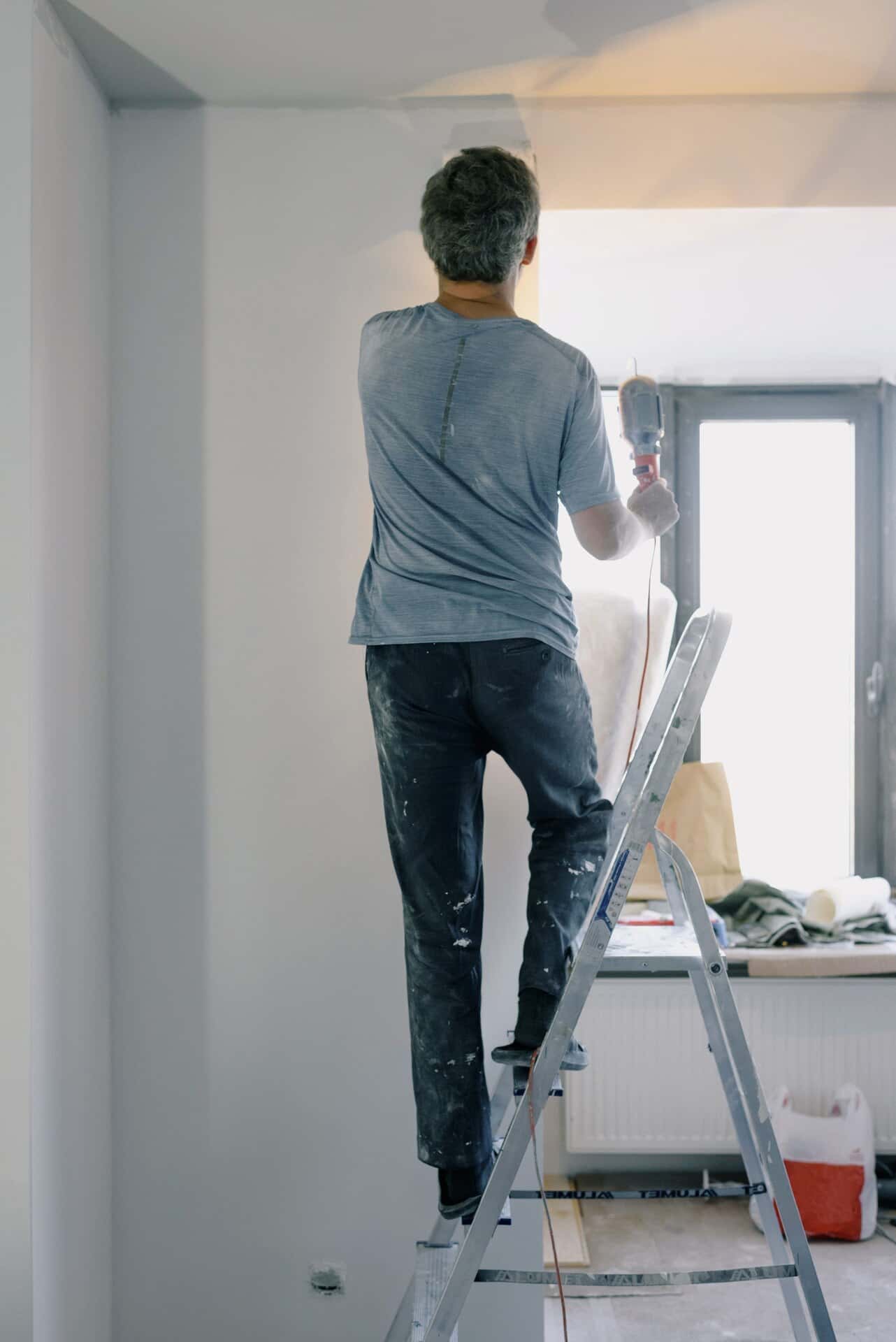 Artisan sur un escabeau, perceuse en main, pendant des travaux dans un appartement