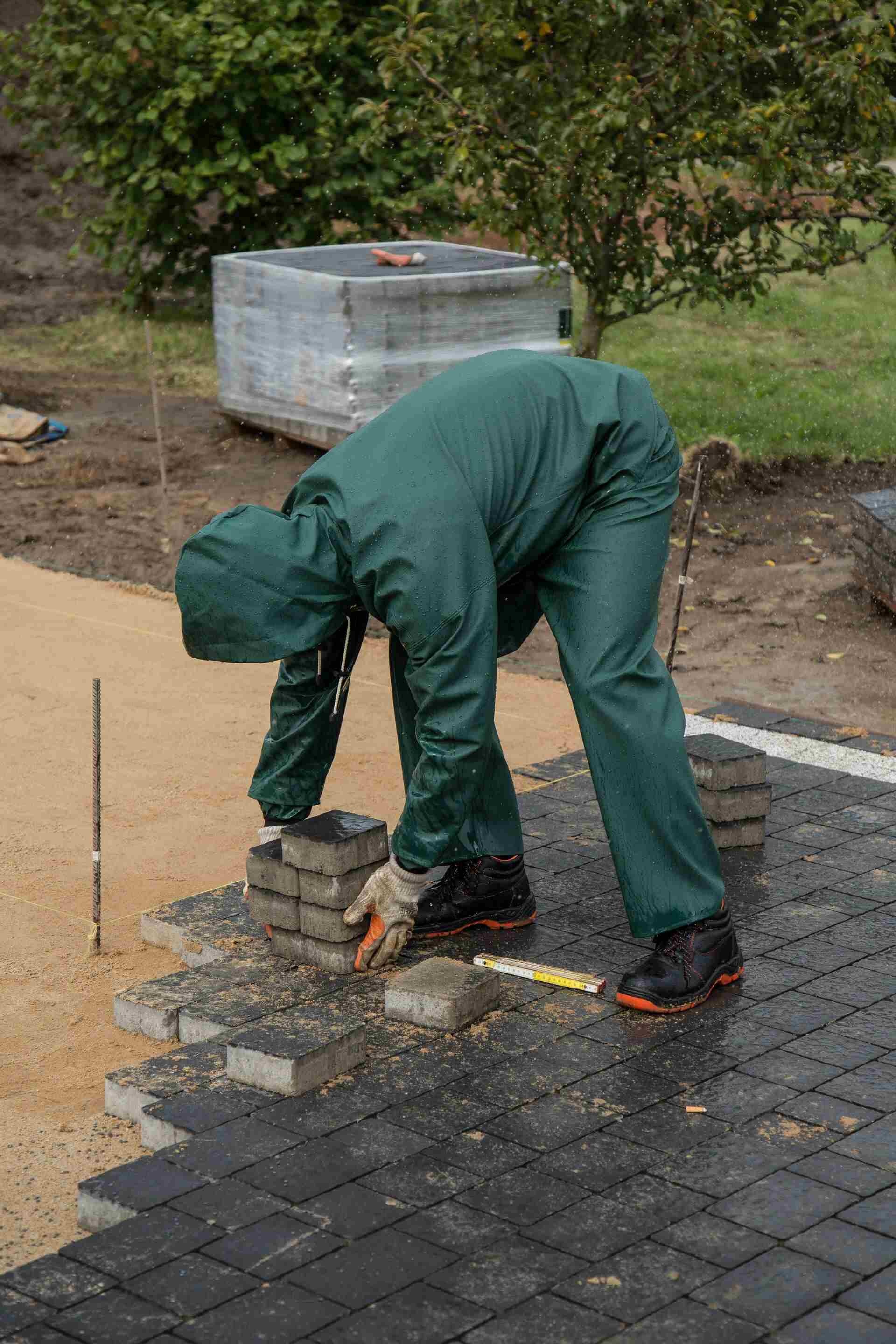 Paysagiste posant des pavés extérieurs, gants et bottes de sécurité, sur un chantier d'aménagement